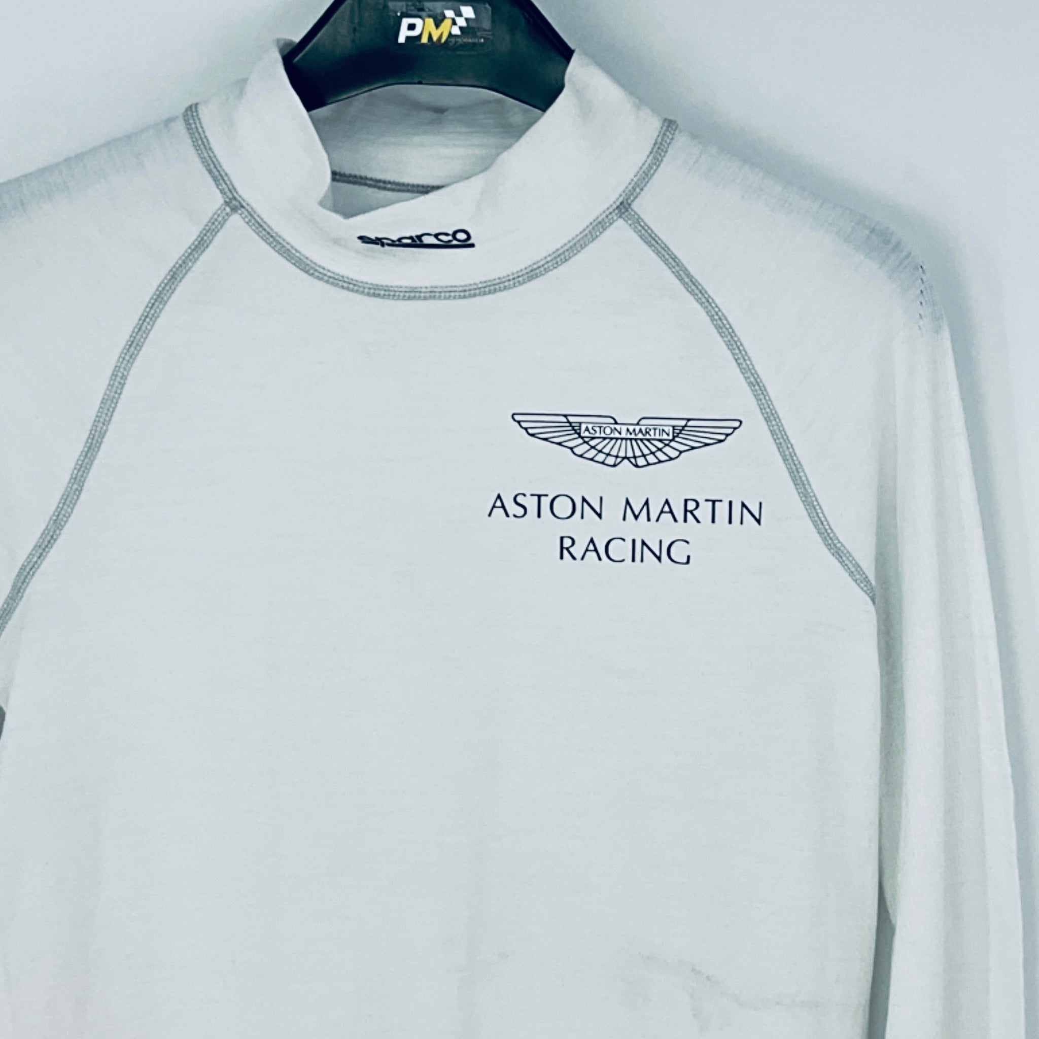 Gray long-sleeve shirt with Aston Martin Racing logo on a hanger.