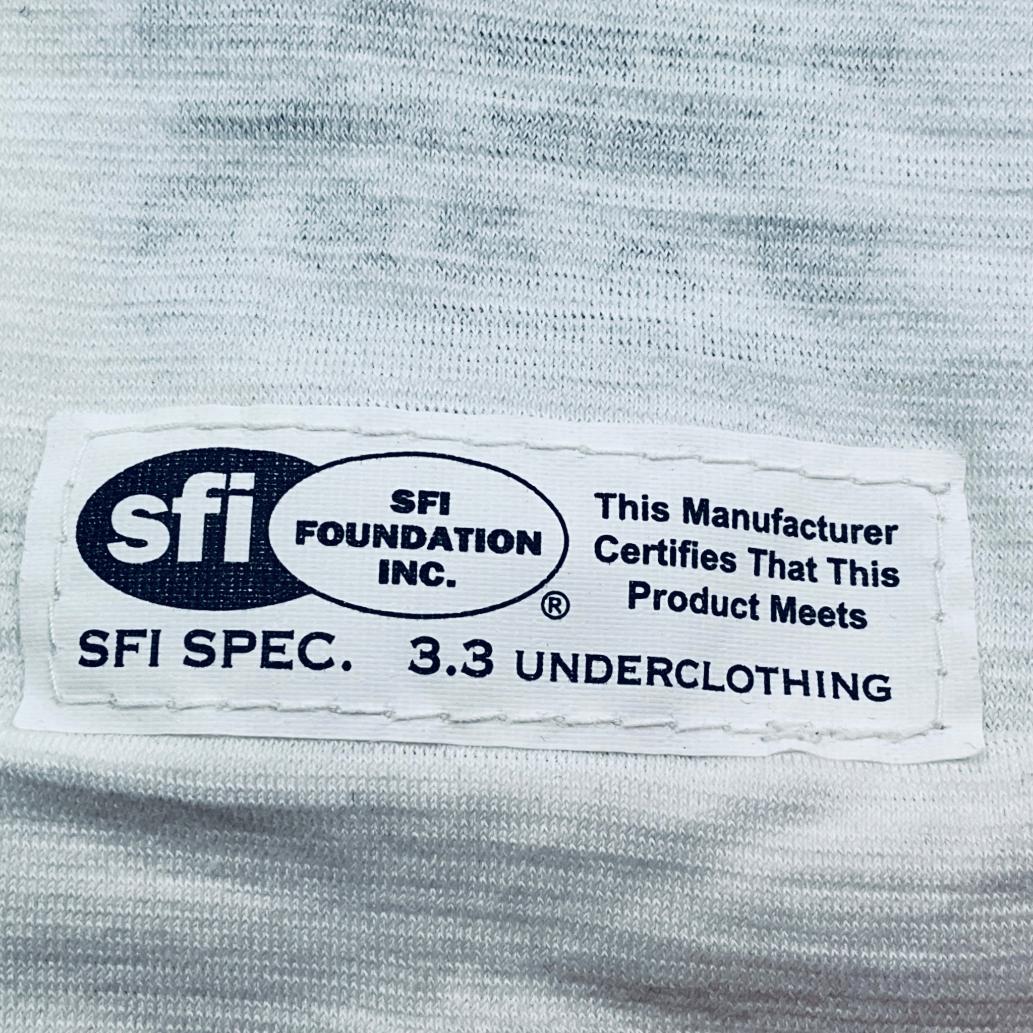 Label on underclothing indicating SFI certification on a gray fabric background