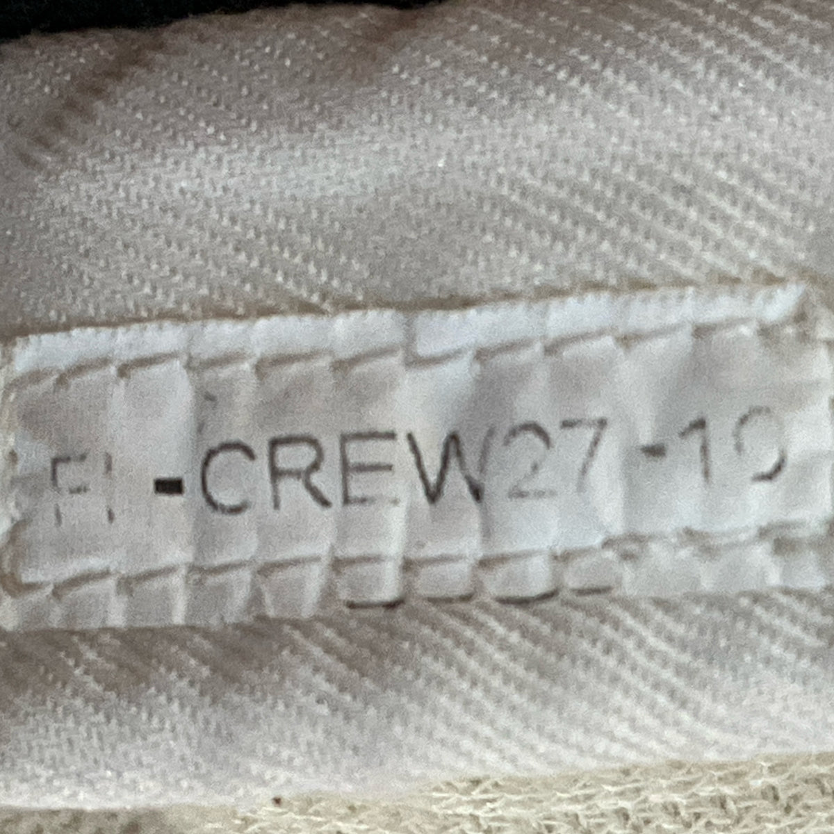 White pit crew suit fabric close-up with printed "F1 -CREW27-17" and stitching