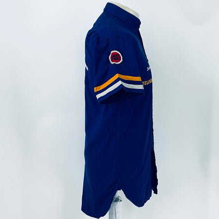 Blue short-sleeve button-up racing shirt side view with small round patch on sleeve
