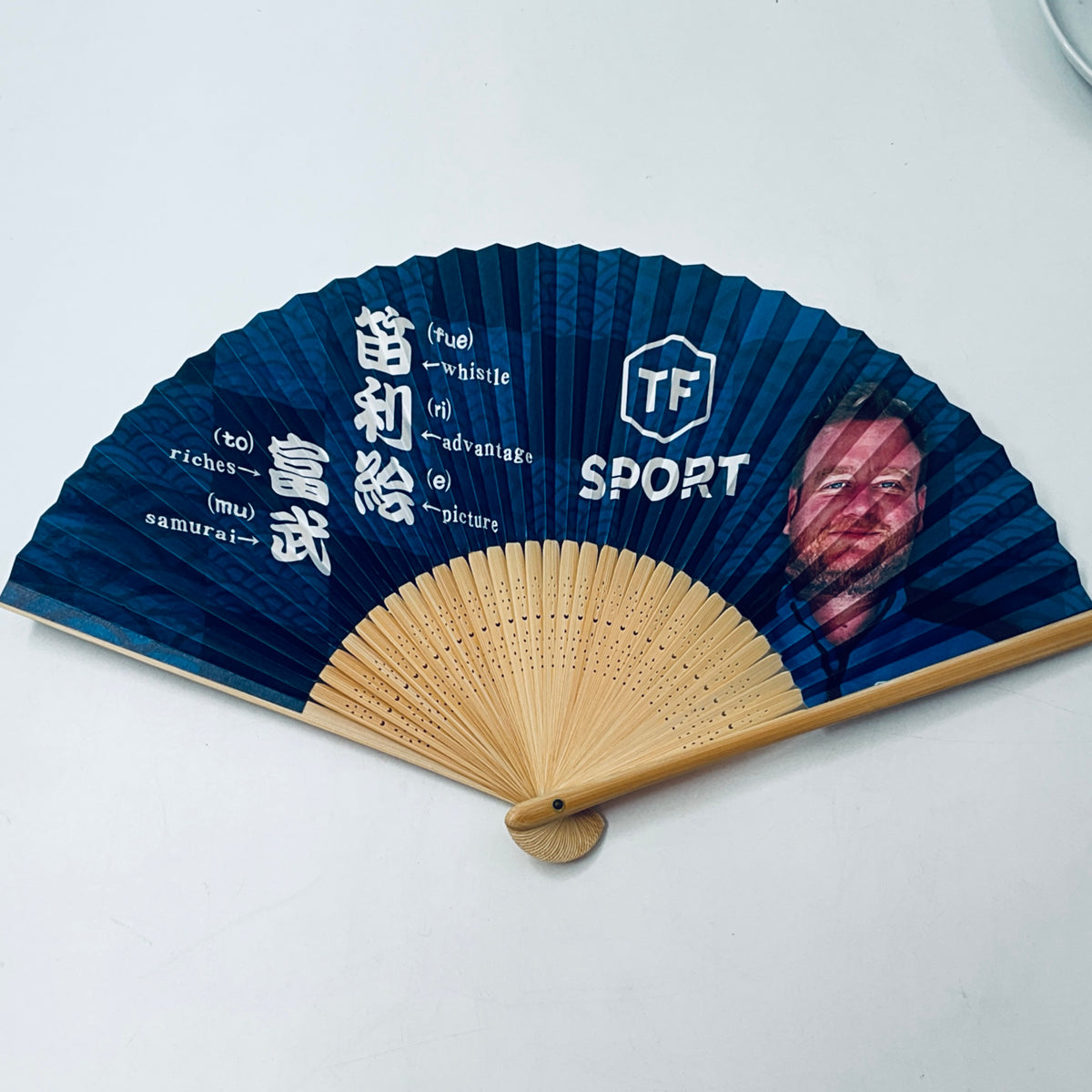 Blue folding fan with wooden handle, SPORT logo and face graphic printed fan blades
