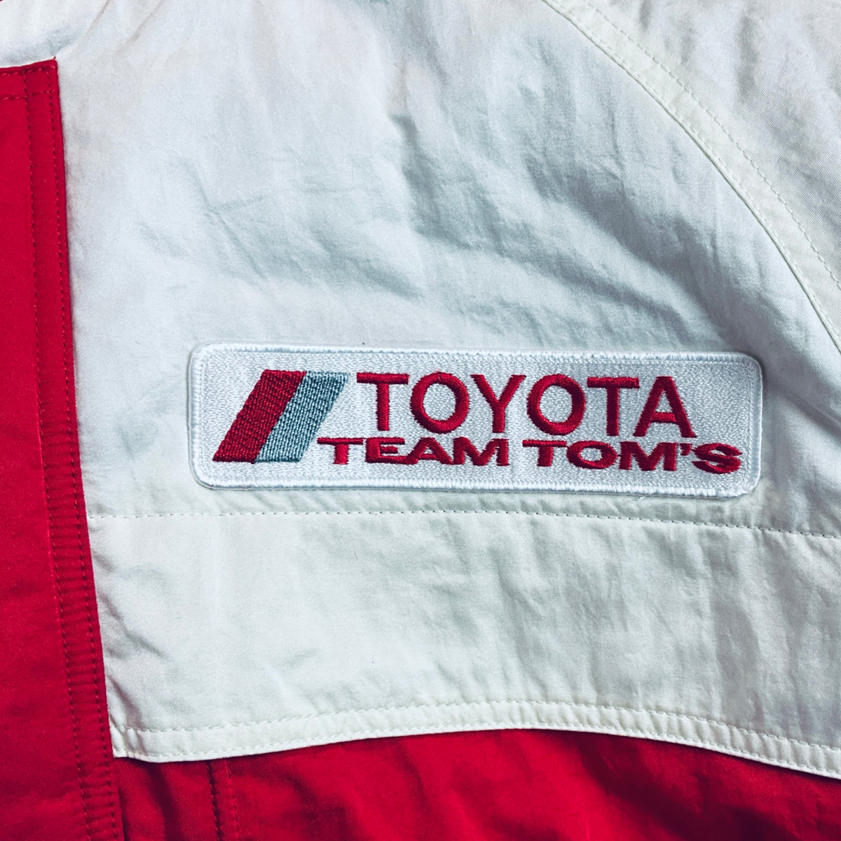 White panel with Toyota Team TOM'S logo patch on red winter jacket