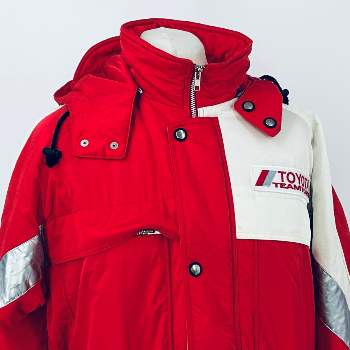 Red winter parka jacket with hood, front zipper, snap pockets, and Team TOM'S patch