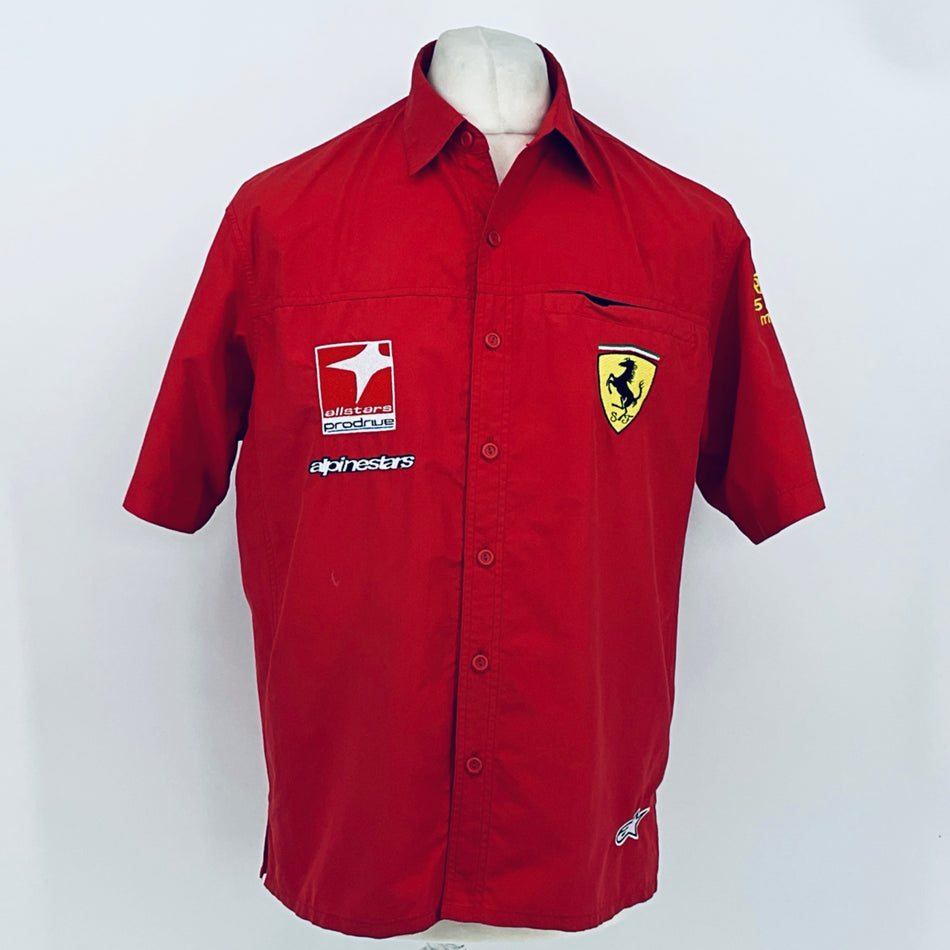 Red racing team polo shirt with Ferrari crest, Alpinestars logo, and front chest badges