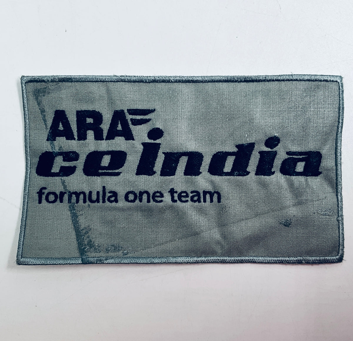 Rectangular gray fabric patch with dark blue 'Formula One team' logo text