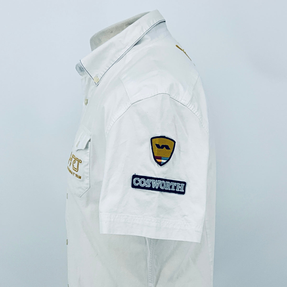 White pit crew shirt viewed from the side, featuring a shield emblem and “COSWORTH” patch.