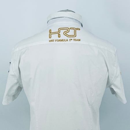 White pit crew shirt back with embroidered “HRT FORMULA 1 TEAM” logo across the shoulders.