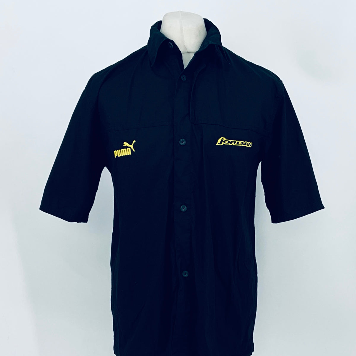 Dark navy short-sleeve button-up shirt with collar; PUMA and JORDAN logos on chest.