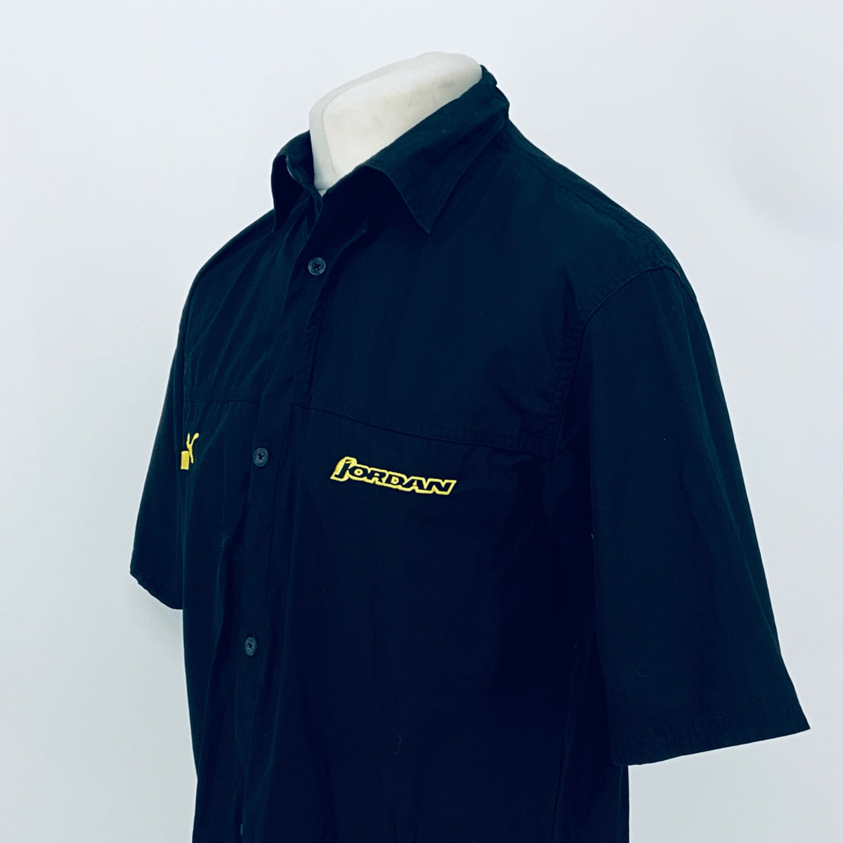 Dark navy short-sleeve button-up shirt, angled view; JORDAN logo patch on chest.