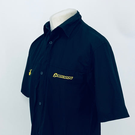 Dark navy short-sleeve button-up shirt, angled view; JORDAN logo patch on chest.
