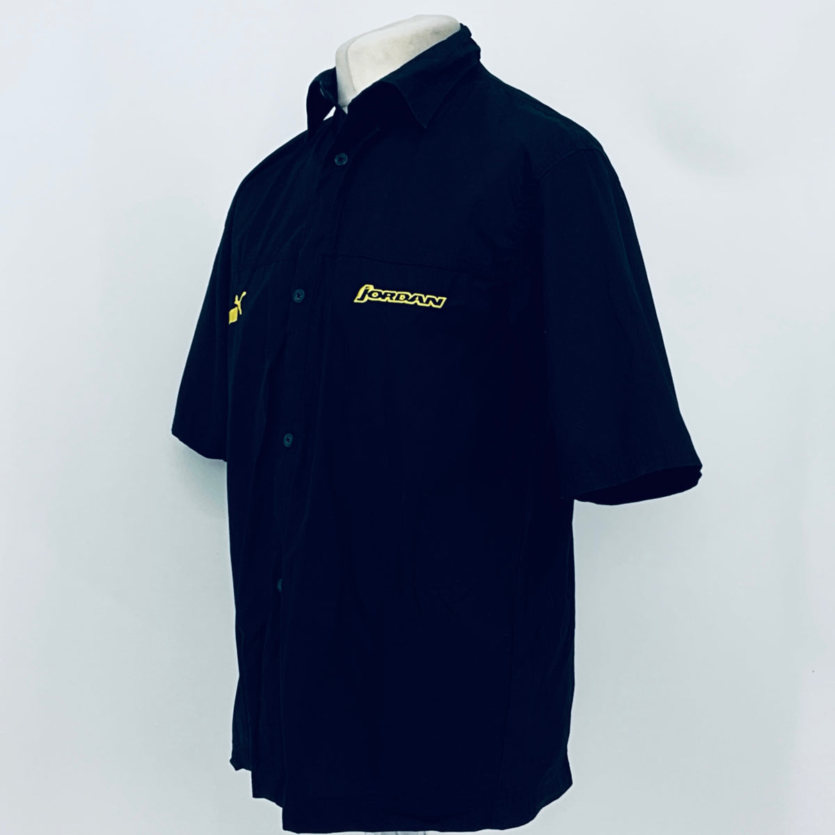 Dark navy short-sleeve button-up shirt, side view; PUMA logo on sleeve and JORDAN chest logo.
