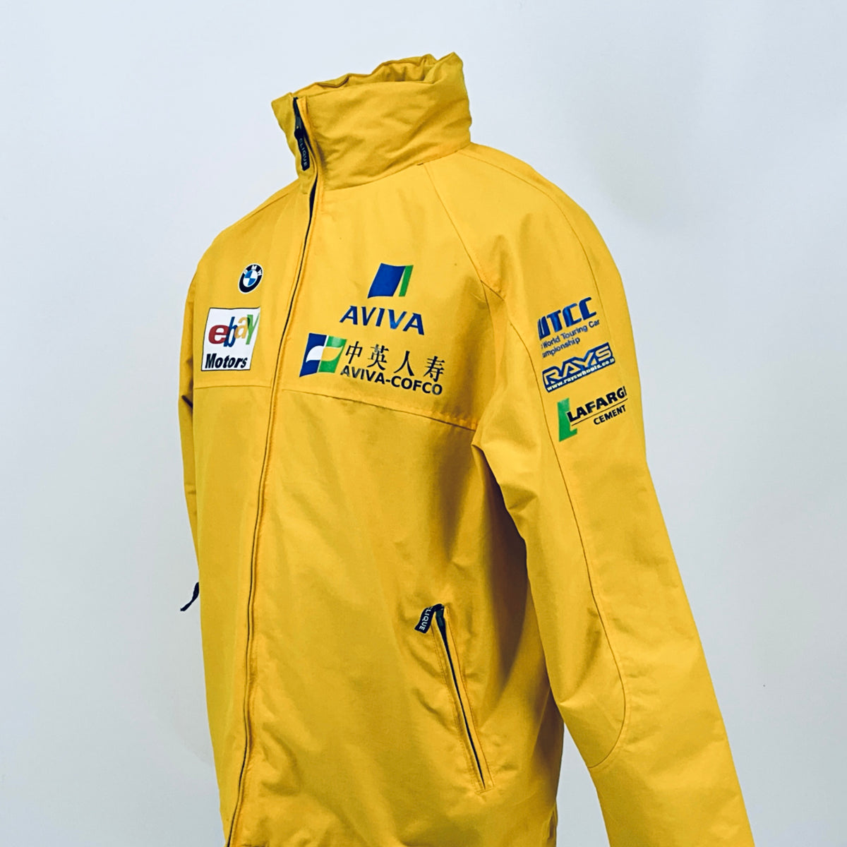 Yellow racing jacket back view with ITC and LAFARGE sponsor logos and hood.