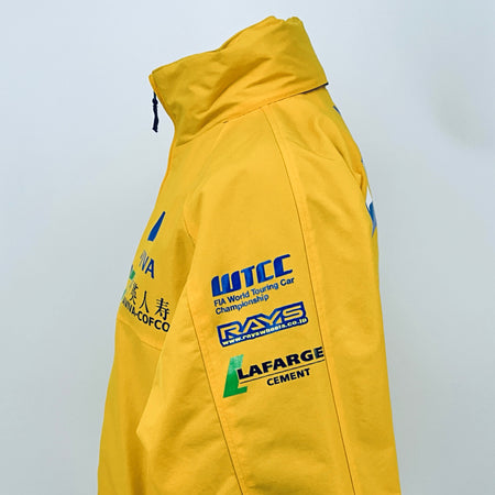 Yellow racing jacket side view with ITC sponsor text and LAFARGE cement patch.