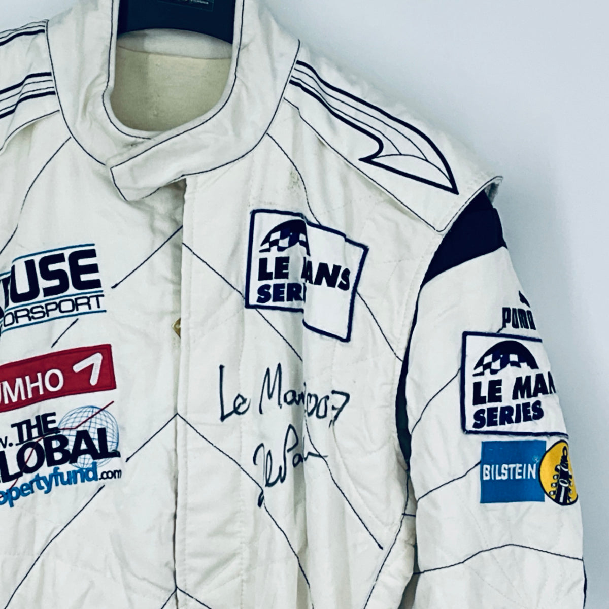 Race-worn driver suit sleeve and chest detail with “Le Mans Series” patch and signatures.