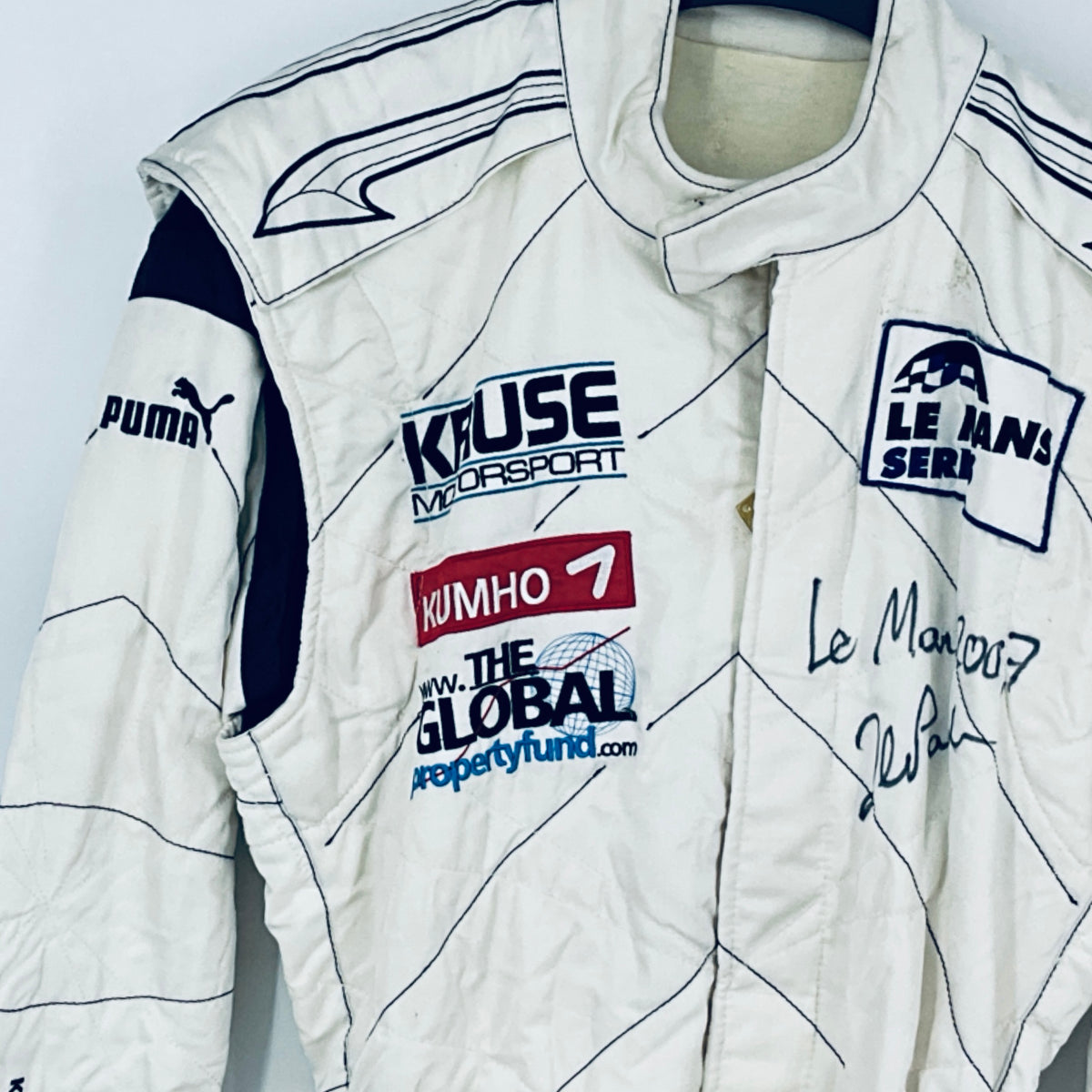 Race-worn driver suit close-up: white fabric with sponsor logos and marker signatures.