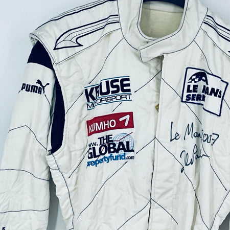 Race-worn driver suit close-up: white fabric with sponsor logos and marker signatures.