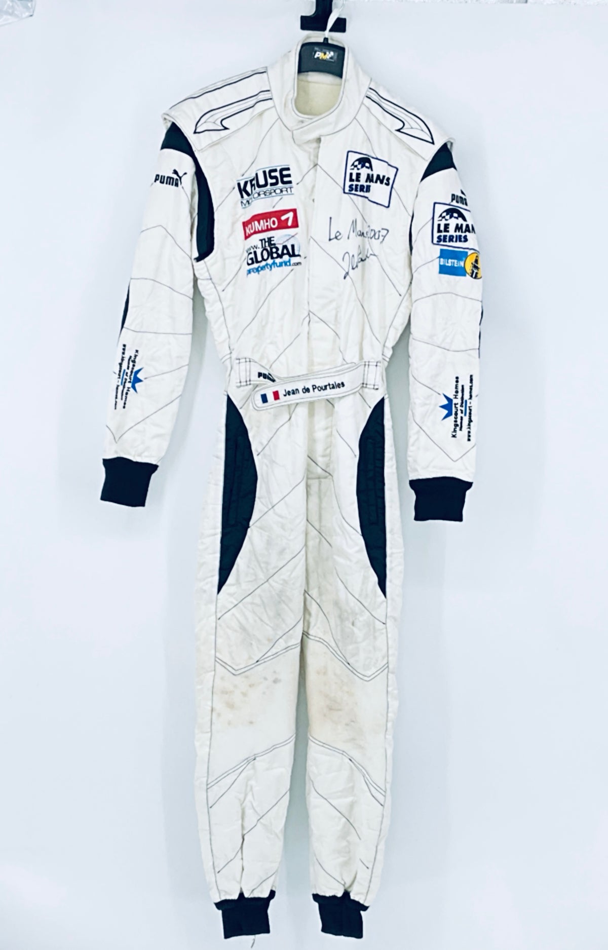 Race-worn driver suit full front view on hanger with sponsor logos and navy cuffs.