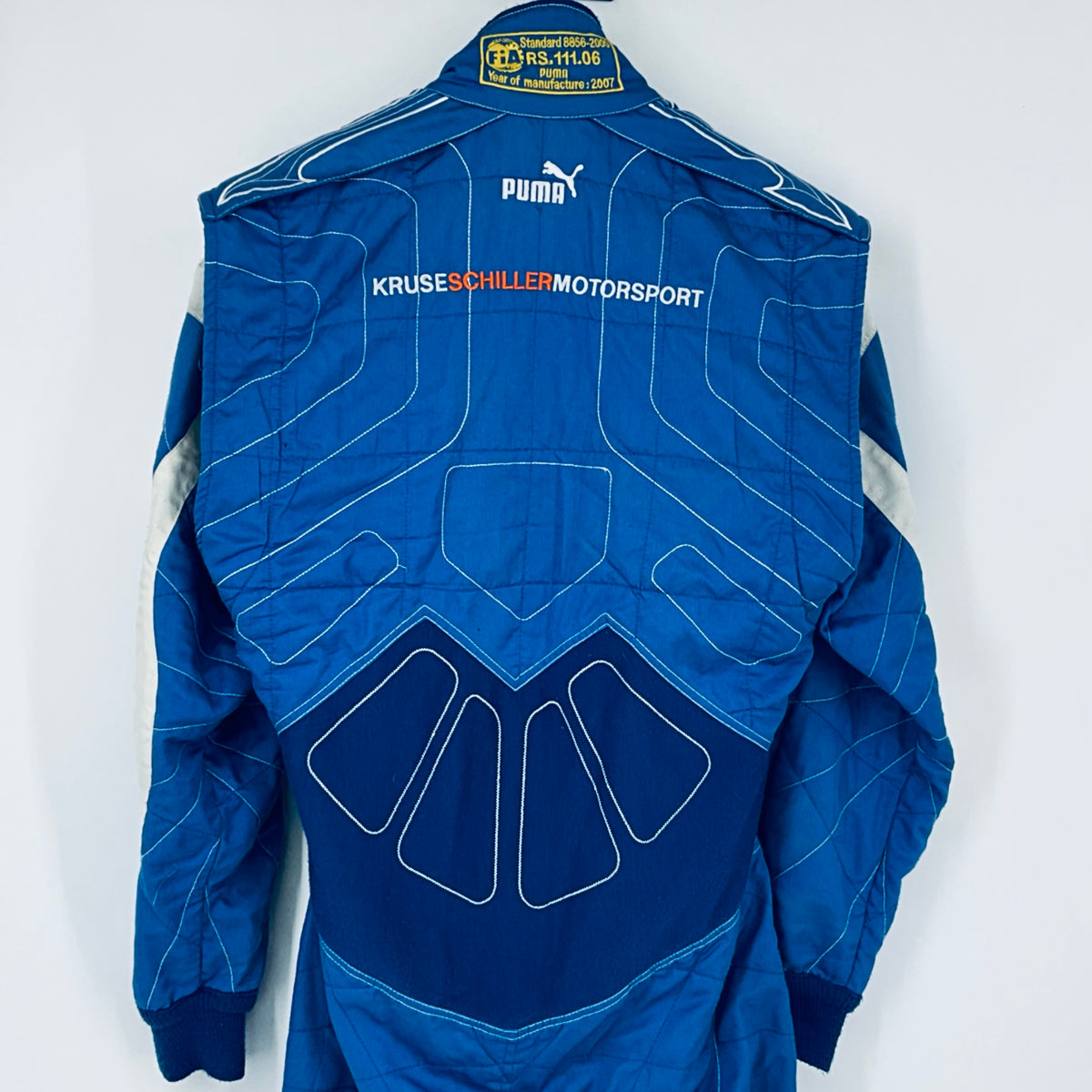 Blue driver suit back with sponsor text, Puma logo, and FIA label at collar
