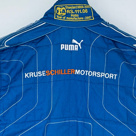 Blue driver suit collar label with FIA text, Puma logo, and KRUSE SCHILLERMOTORSPORT