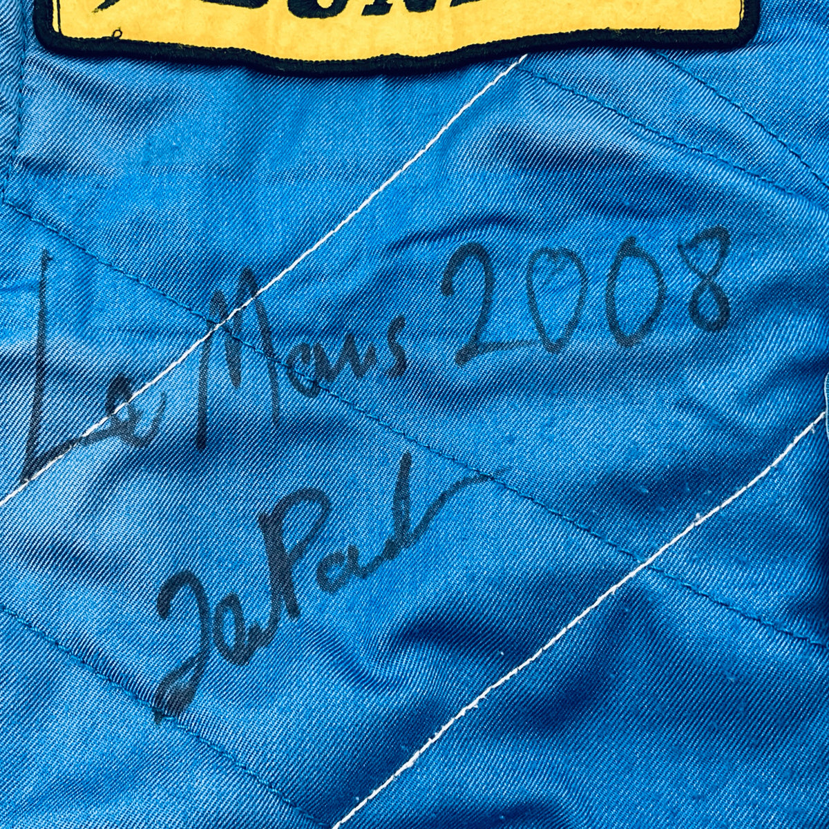 Handwritten autograph on blue quilted driver suit panel