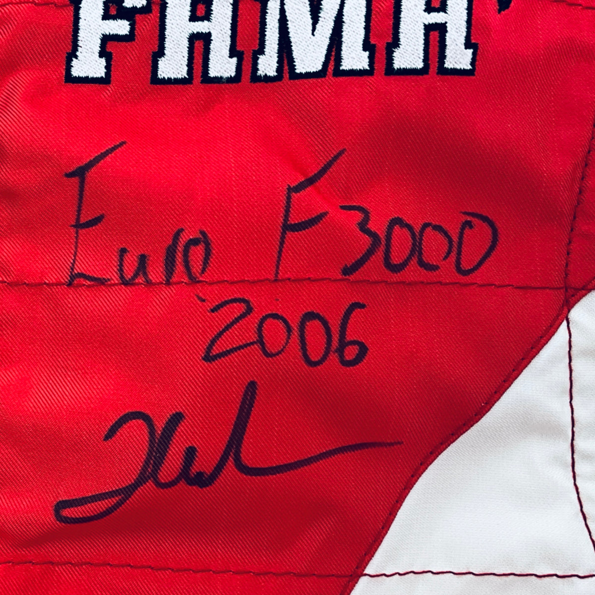 Red driver suit panel with black marker signatures and “FHM” lettering