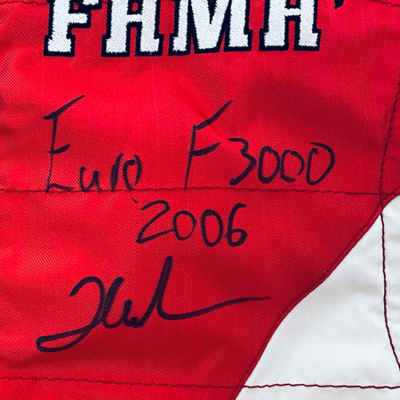Red driver suit panel with black marker signatures and “FHM” lettering