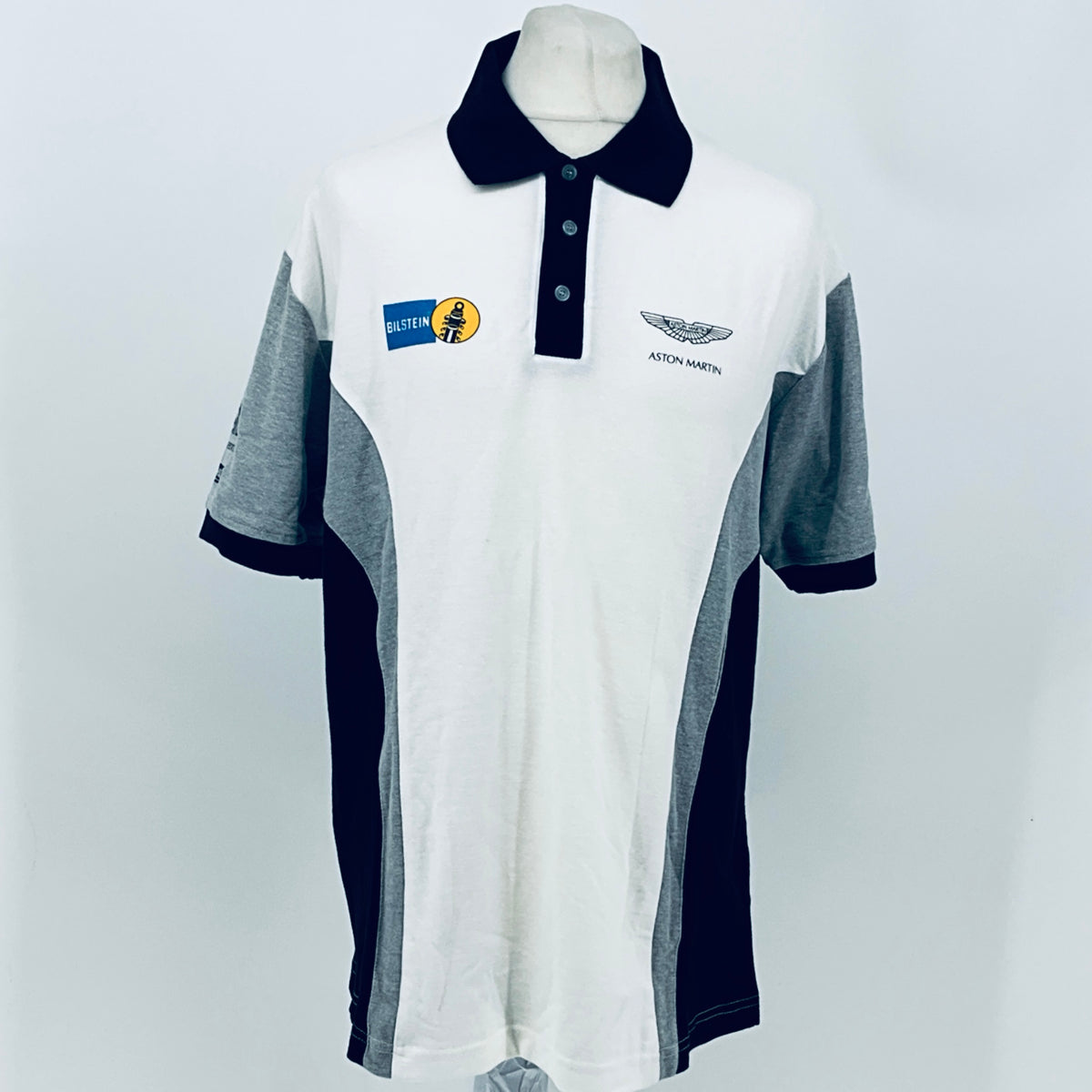 White polo shirt with navy collar, button placket, gray sleeves, front team logos