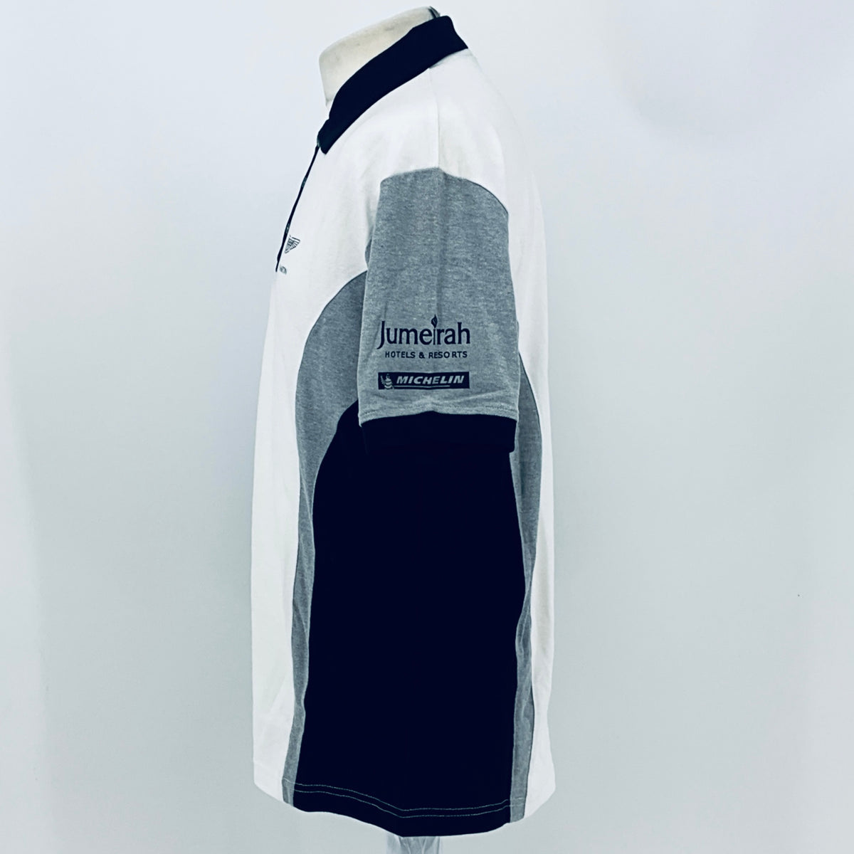 Side view of white polo shirt with navy collar and gray sleeve panel, Jumeirah & MICHELIN branding