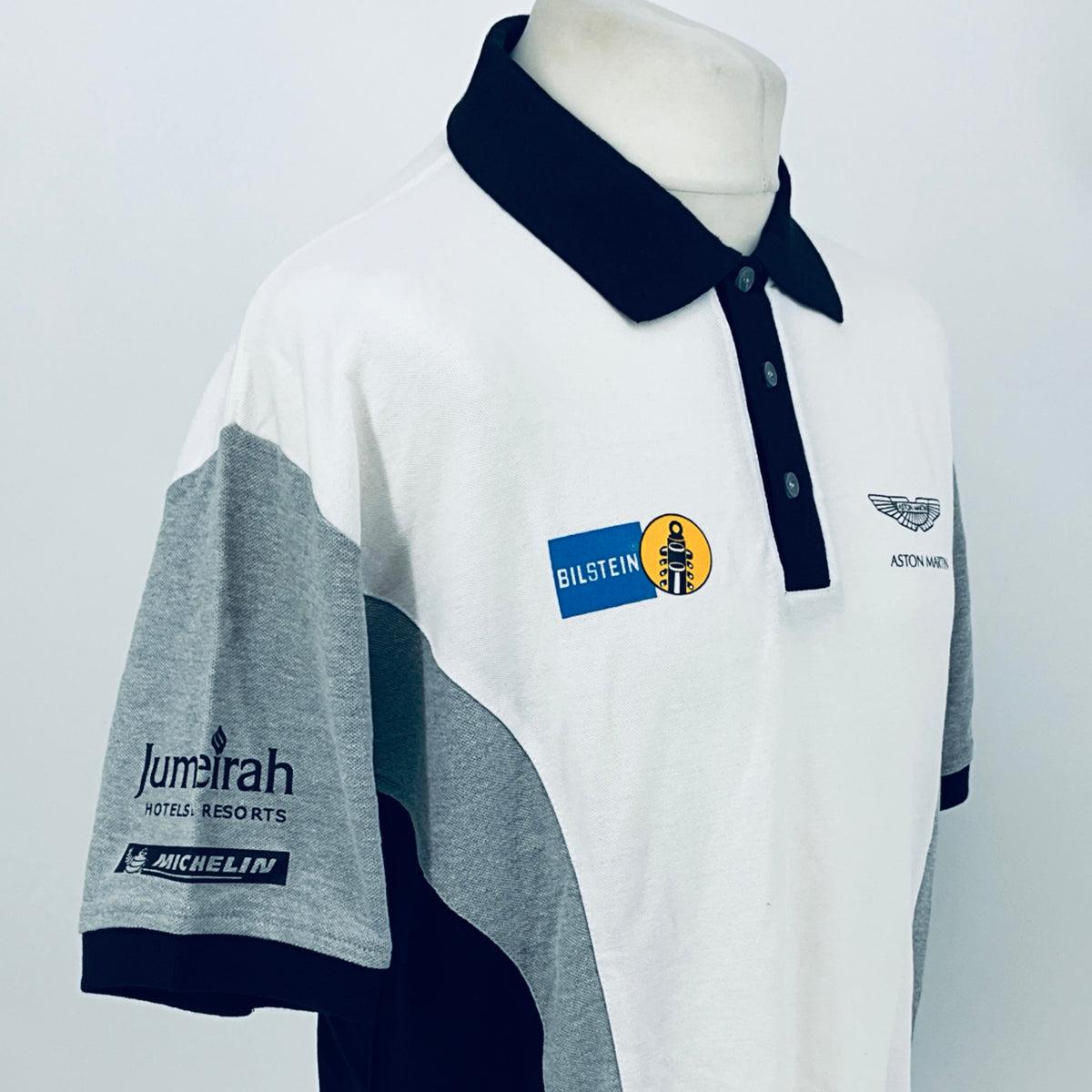 White polo shirt with navy bow collar, logos, and gray left sleeve panel