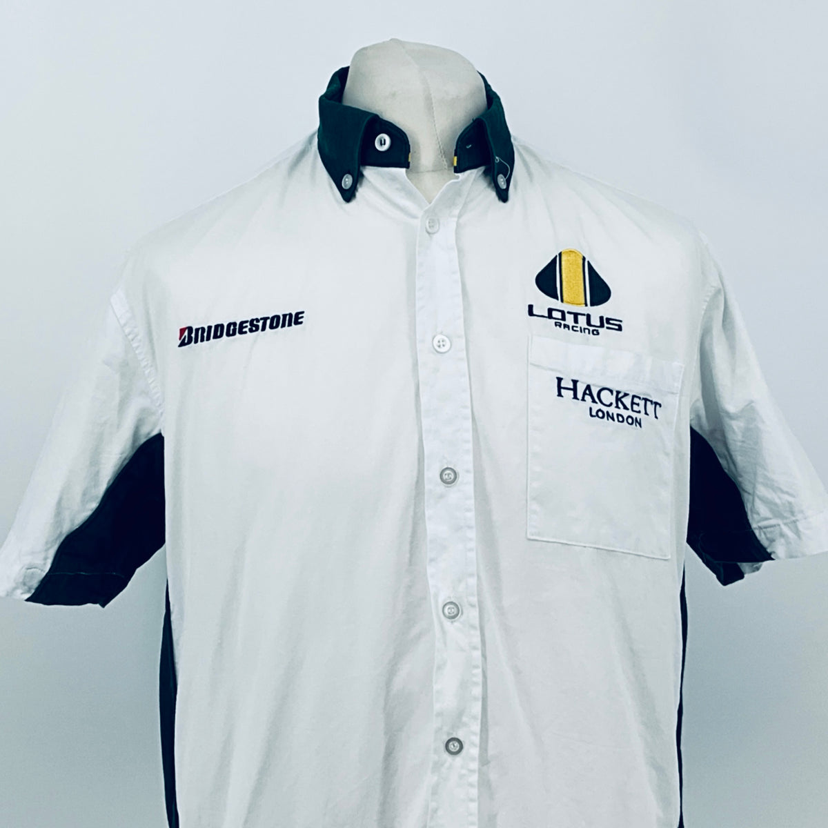 White short-sleeve button shirt with dark collar, chest pocket, and racing logos