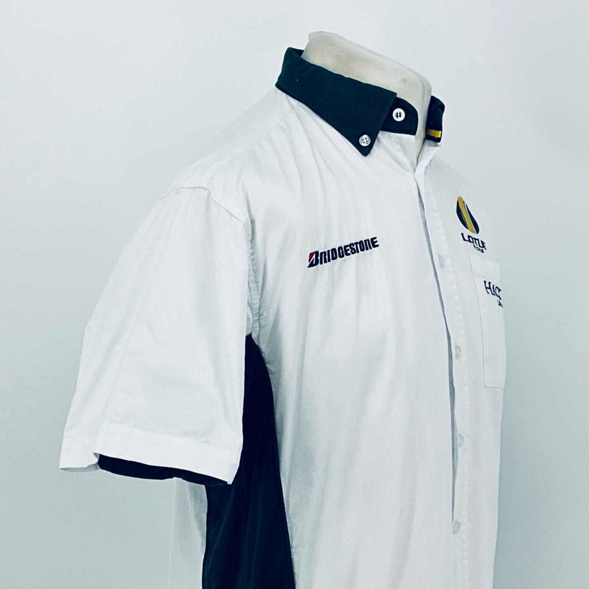 White short-sleeve button shirt with dark collar and chest logo on angled view