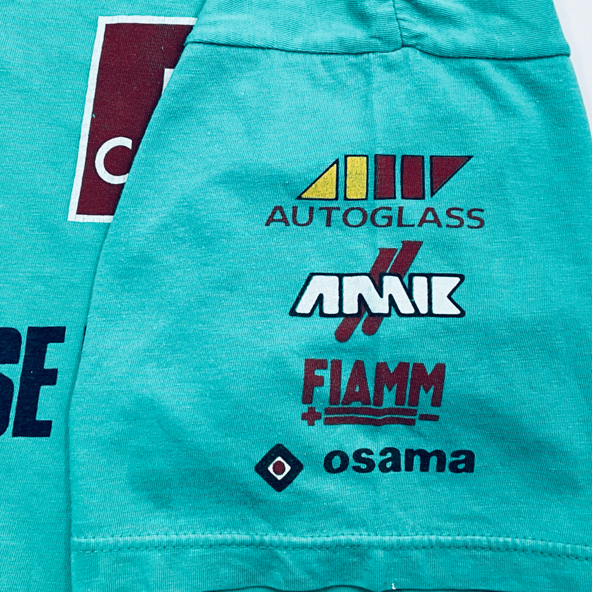 Teal jacket with logos of Autoglass, Amik, Fiamm, and Osama on a white background